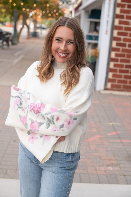 Woman holding a floral-patterned bag on a street with brick buildings and trees in the background