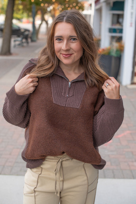 Woman wearing a brown sweater with a contrasting collar on a street.