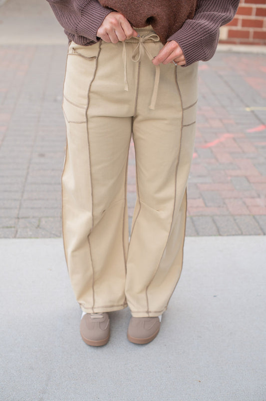 Person wearing beige pants and a brown sweater on a pavement background