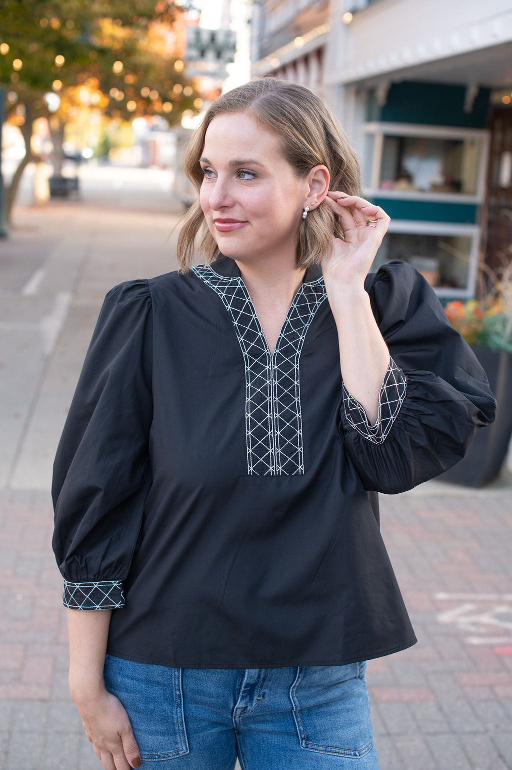 Woman wearing a black blouse with intricate white embroidery on a city street.