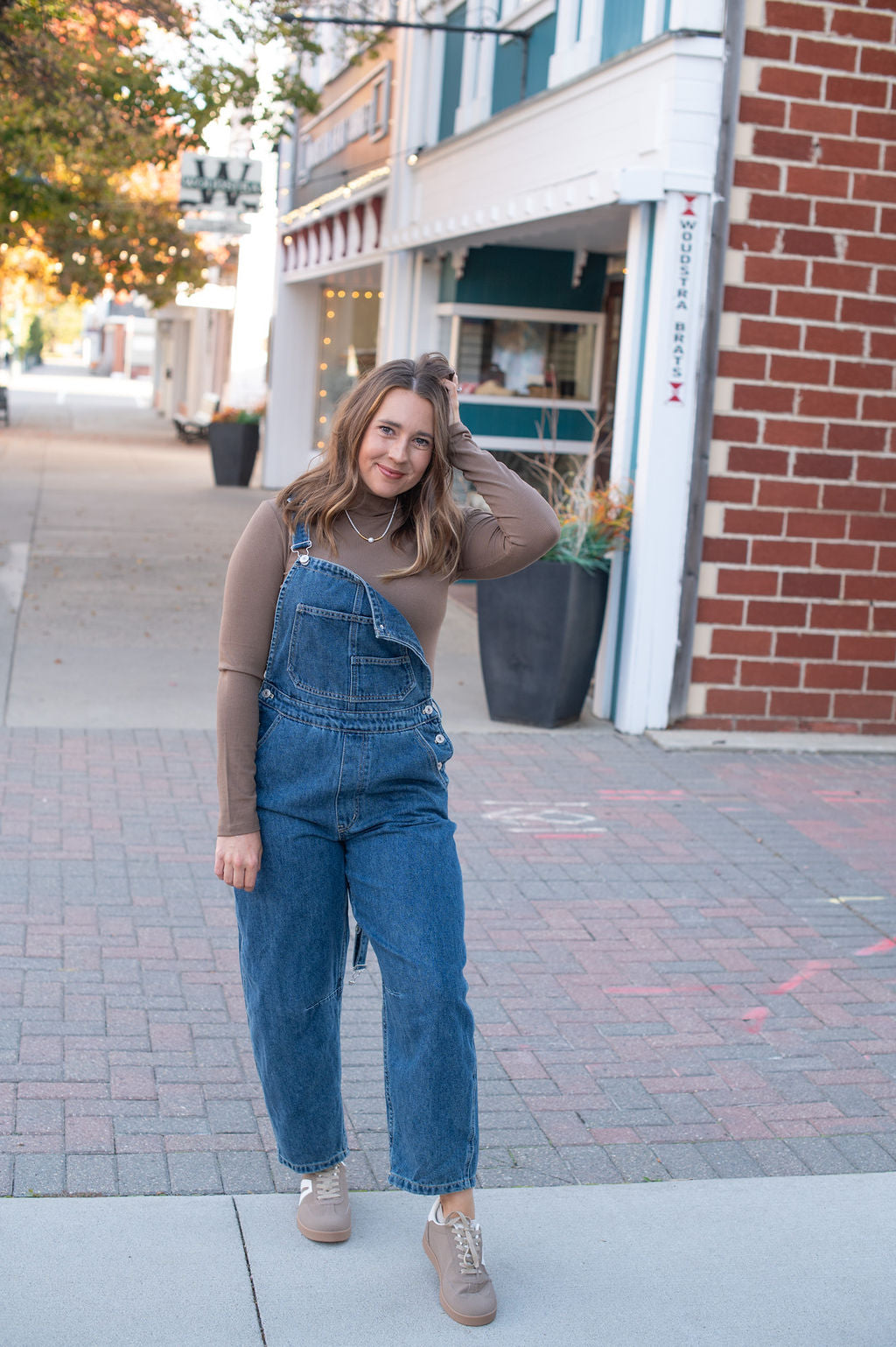 Woman wearing blue denim overalls standing on a sidewalk with buildings in the background
