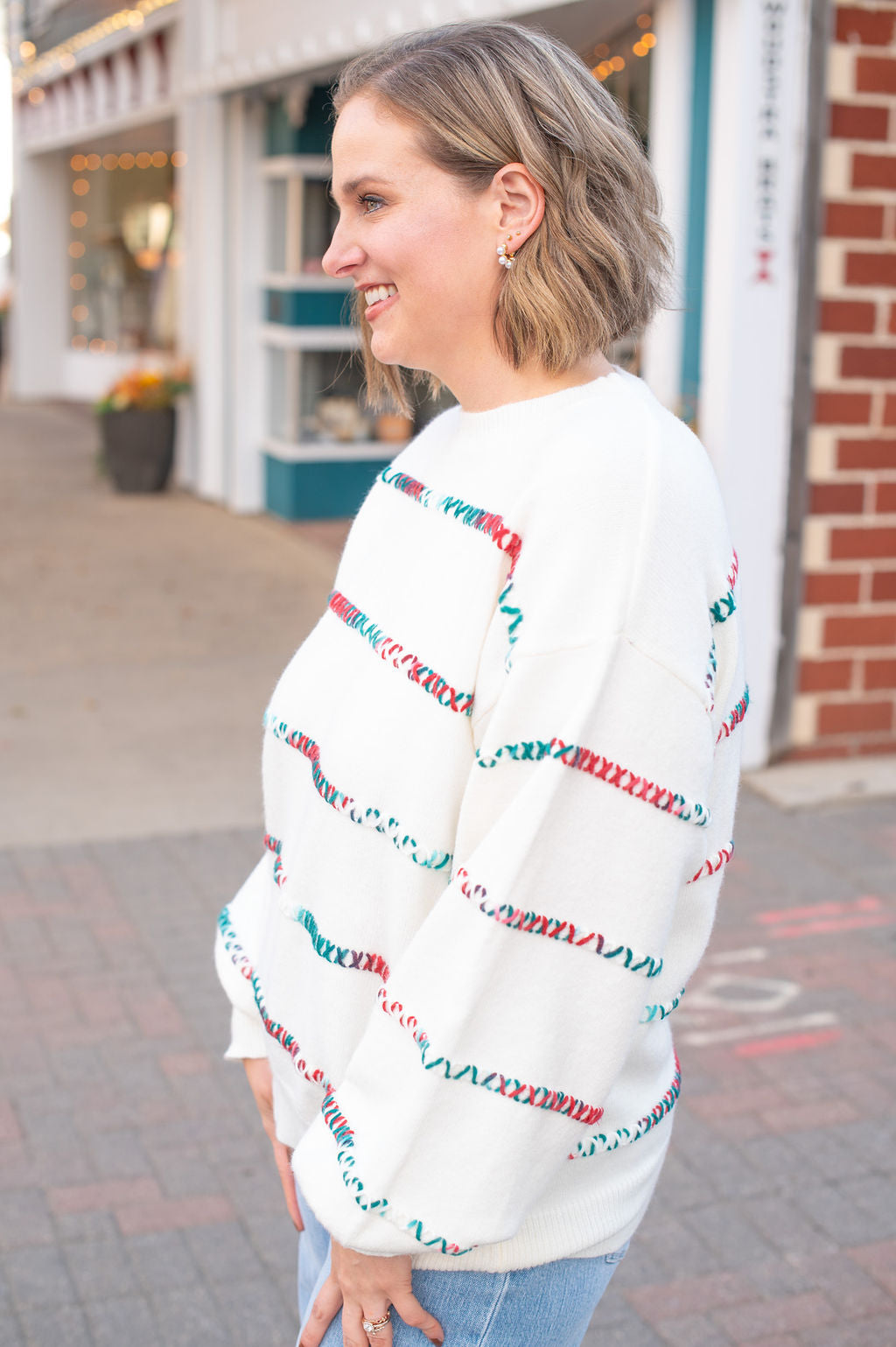 Woman wearing a white sweater with colorful patterns standing on a street.