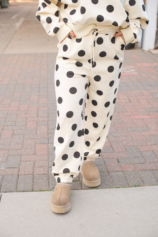 Person wearing cream polka dot pants and beige boots on a paved surface