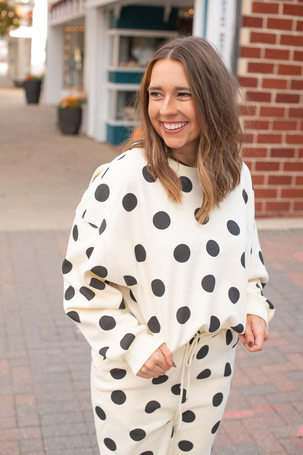Woman wearing a polka dot outfit standing on a sidewalk with brick buildings in the background.