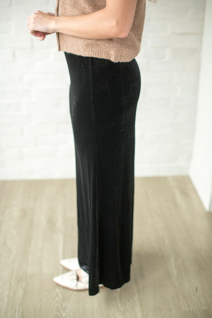 Person wearing a beige sweater and black pants on a plain background