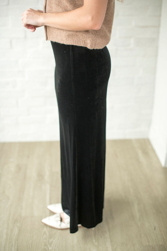 Person wearing a beige sweater and black pants on a plain background