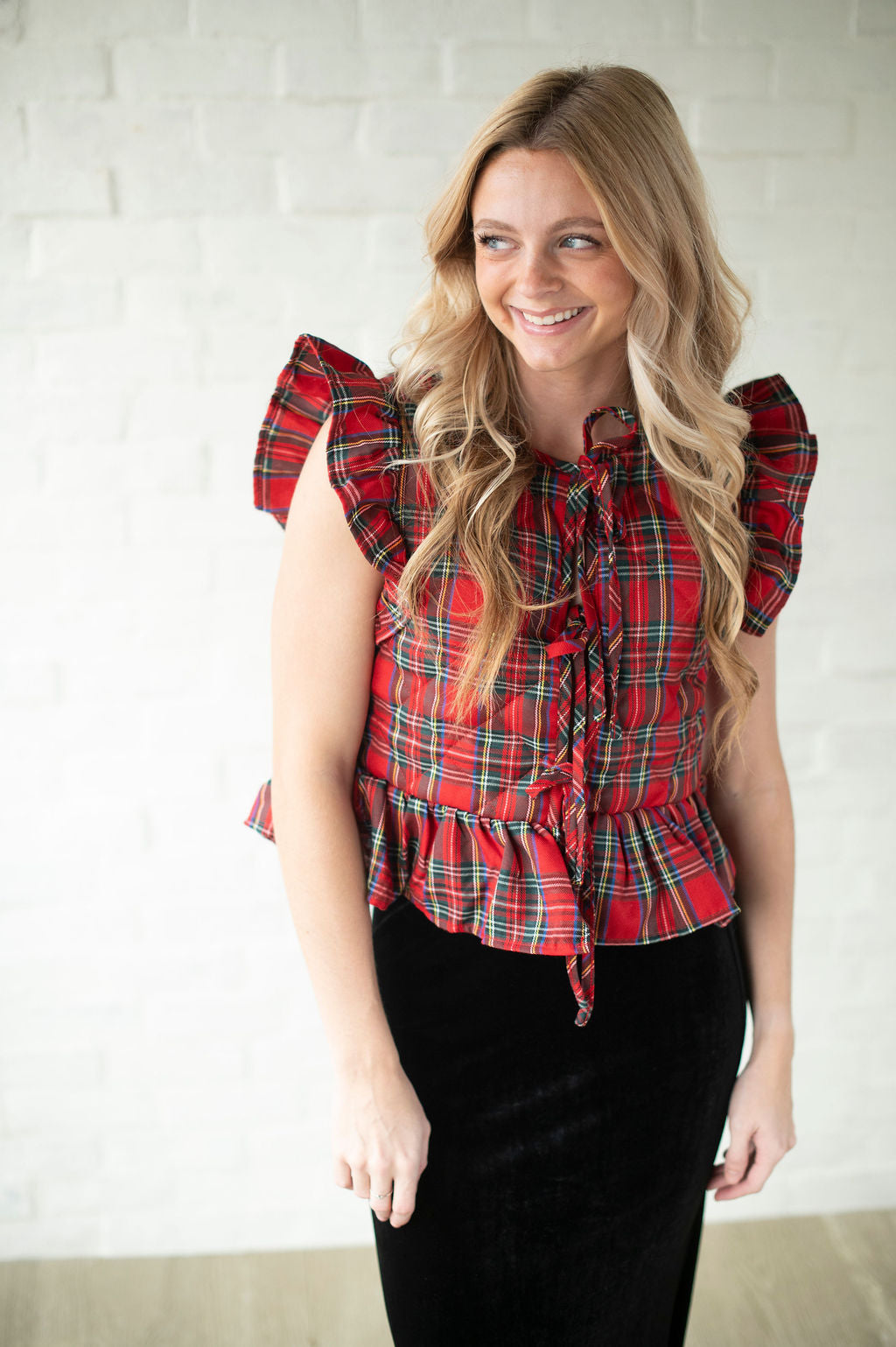 Woman wearing a red plaid top with ruffled sleeves against a white wall.