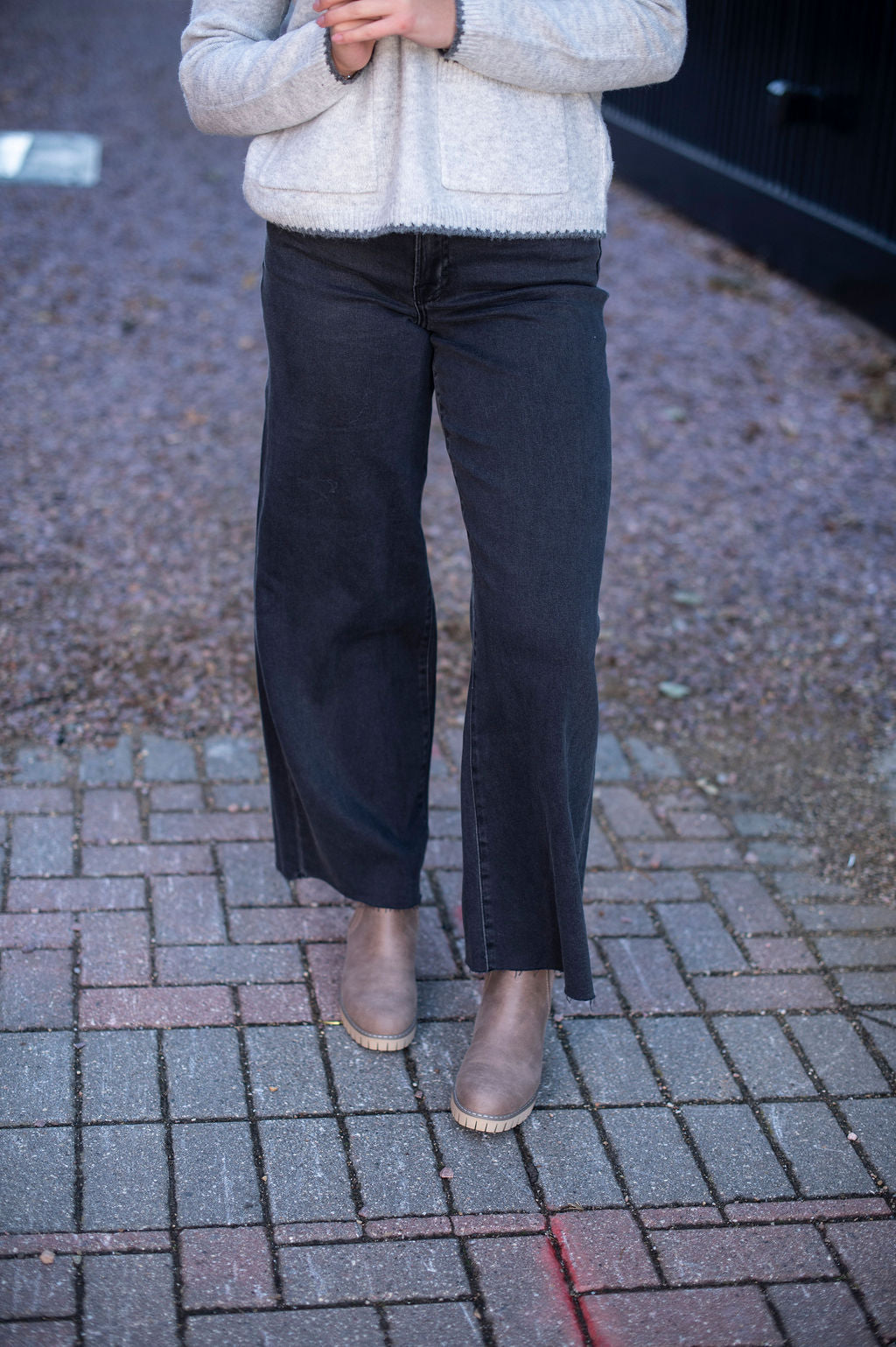 Person wearing a light gray sweater and dark pants on a brick pavement.