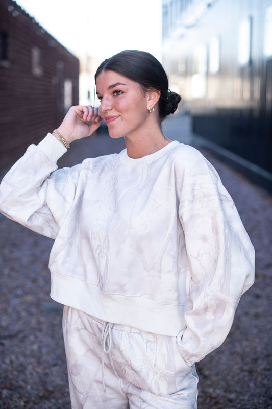Woman wearing a white camo outfit standing outdoors.